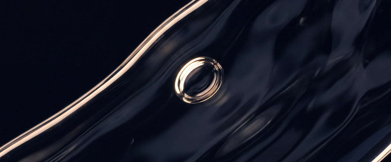 Macro de líquido viscoso escuro em fluxo, com uma bolha de ar redonda presa e luz rasante desenhando a borda.