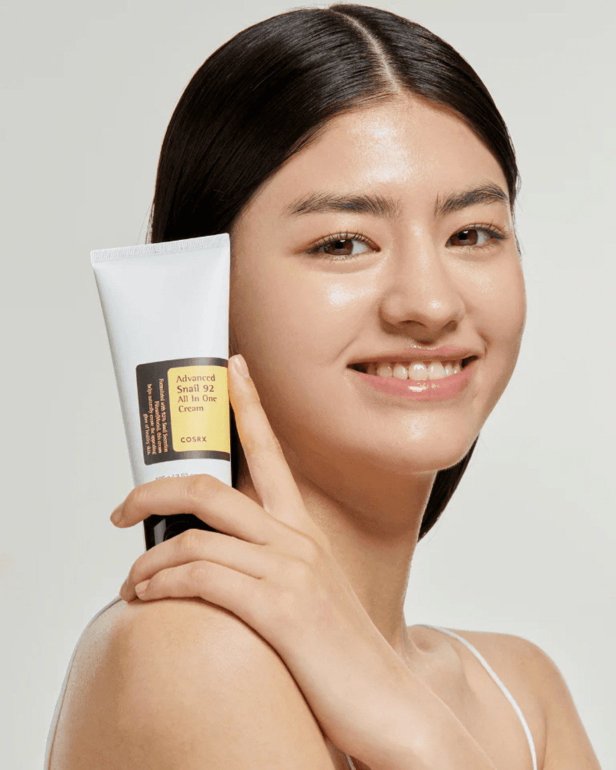 Modelo segura a bisnaga do creme COSRX Advanced Snail 92 All In One Cream junto ao rosto