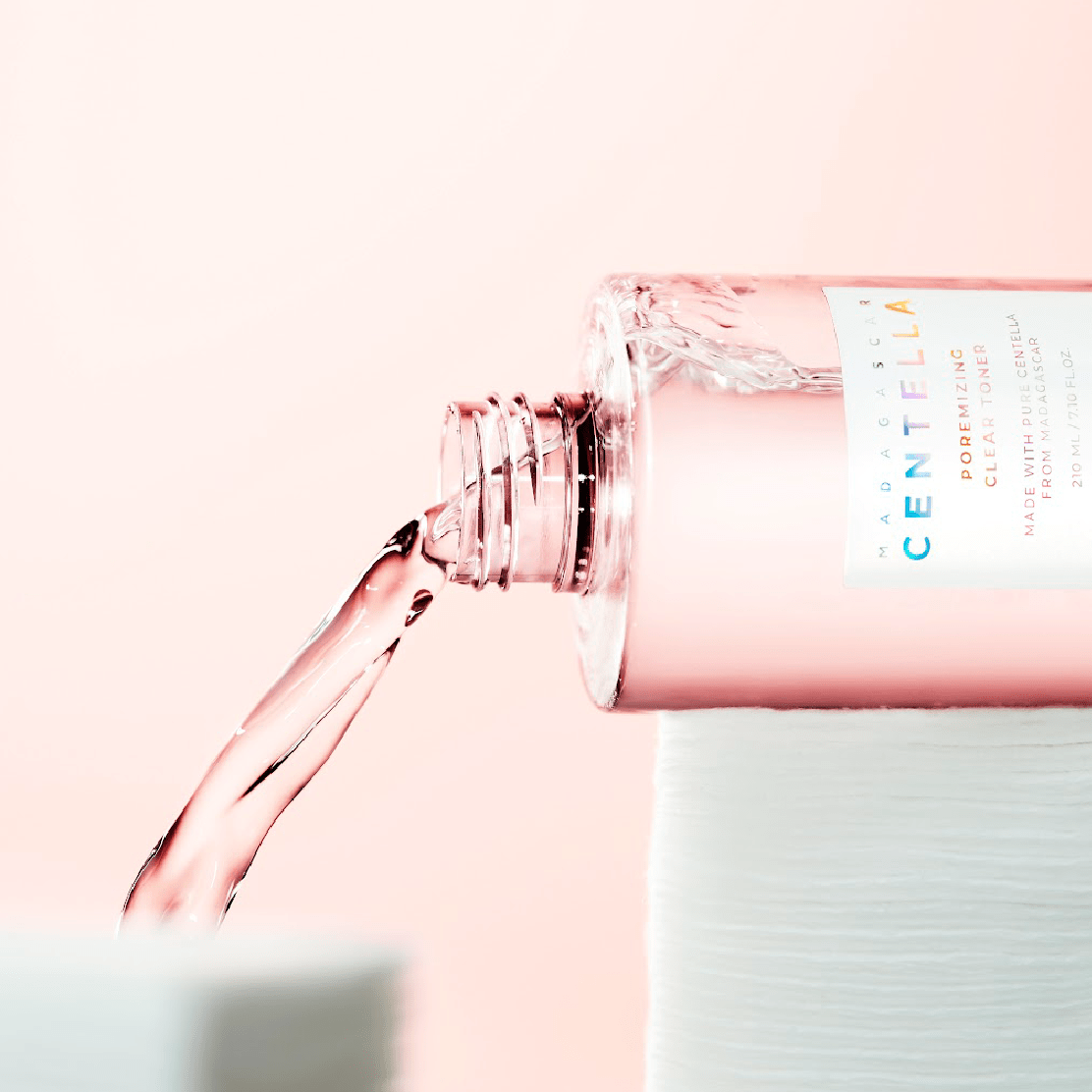 Frasco deitado despejando o liquido rosa ao lado de discos de algodao