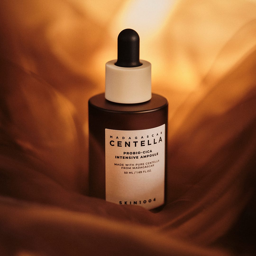 Frasco ambar da SKIN1004 Madagascar Centella Probio-Cica Intensive Ampoule de 50 ml apoiado sobre tecido dourado