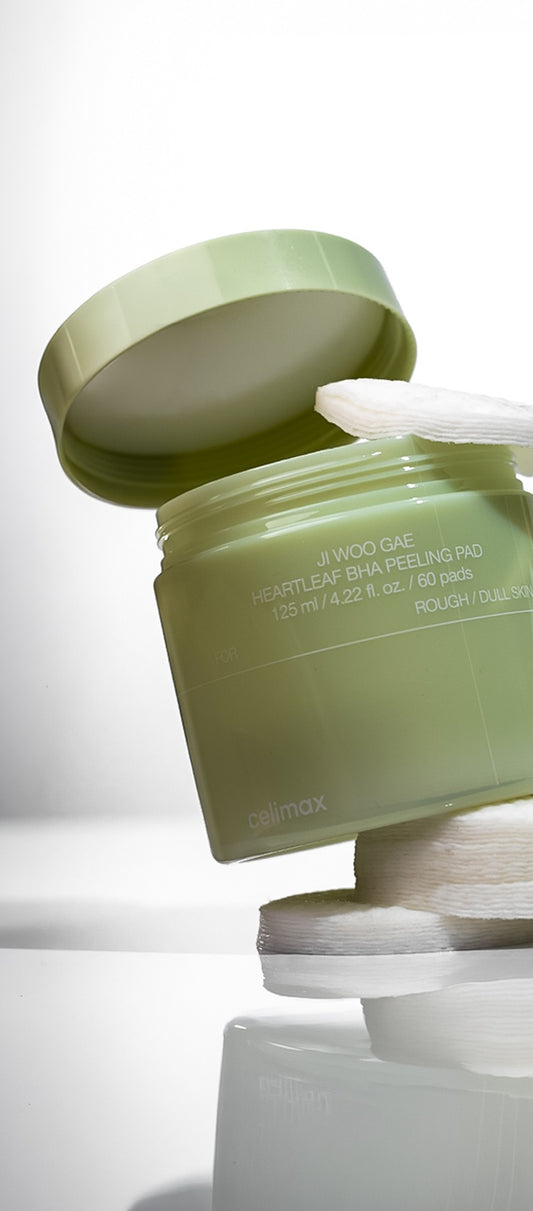 Pote verde do Celimax Ji Woo Gae Heartleaf BHA Peeling Pad aberto, com discos de algodao empilhados, fundo claro.