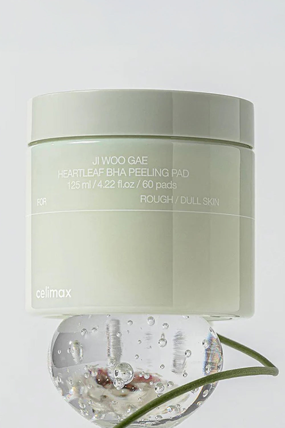 Pote verde fechado do Celimax Ji Woo Gae Heartleaf BHA Peeling Pad apoiado sobre uma esfera de gel transparente.