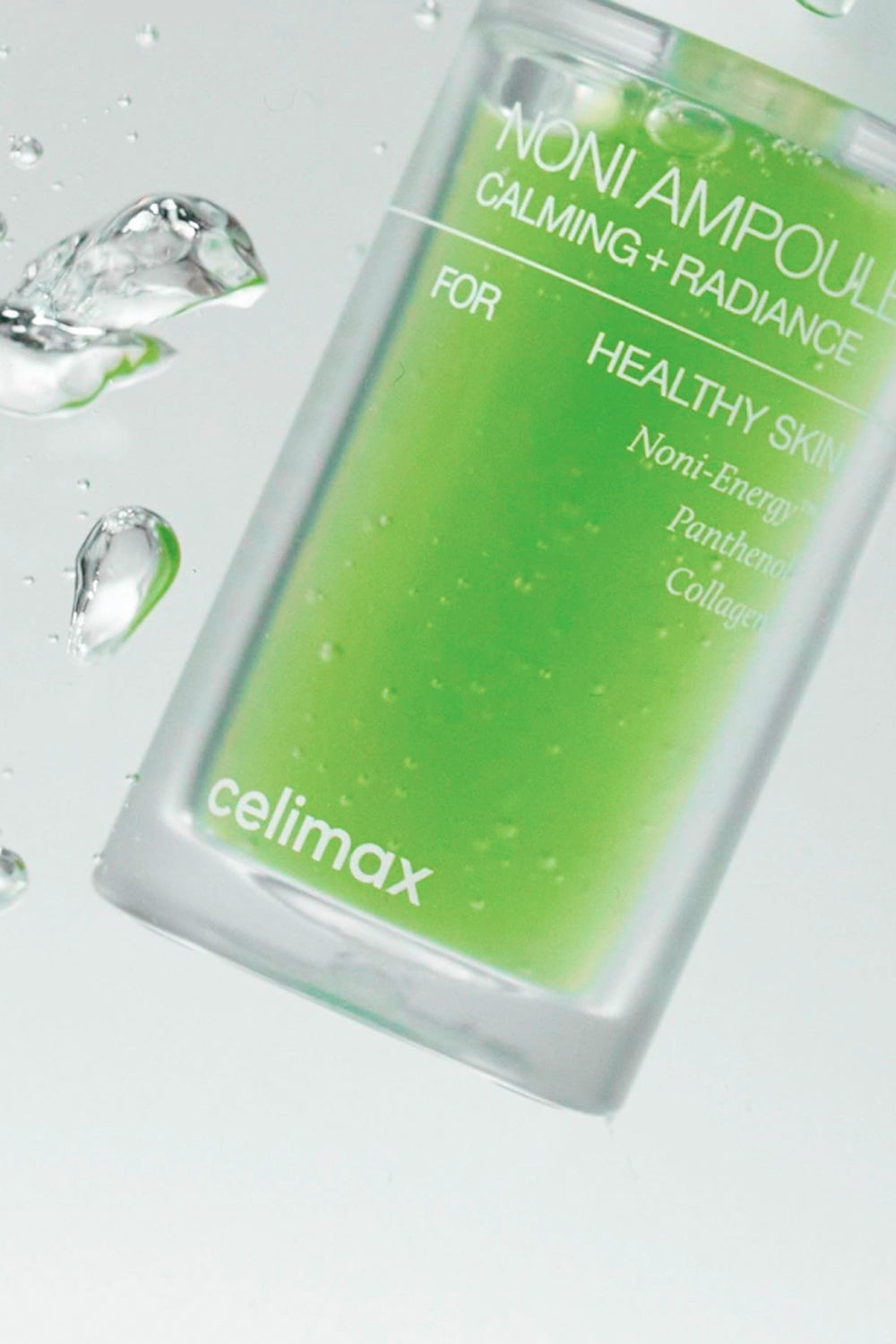 Close do frasco verde da ampola Noni da Celimax com respingos de liquido transparente ao redor.