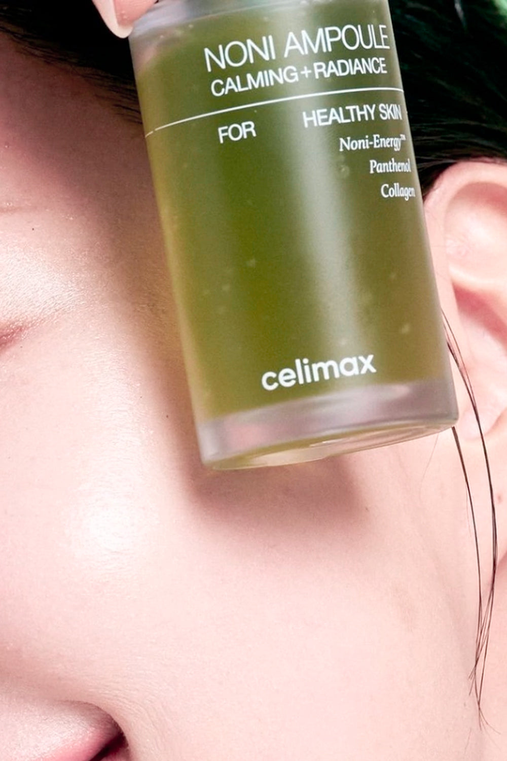 Frasco verde da ampola Noni da Celimax em primeiro plano, encostado no rosto de uma modelo.