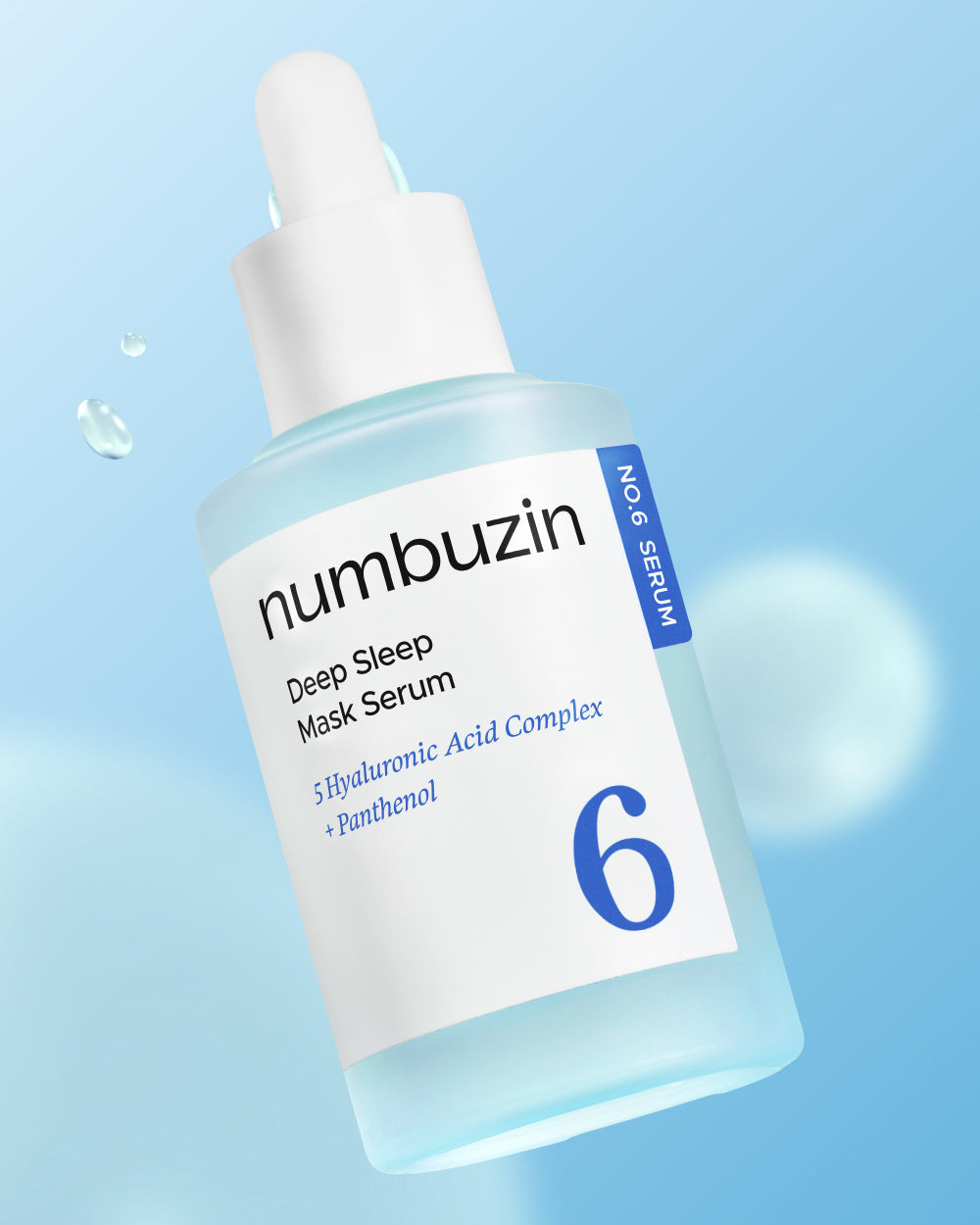 Frasco de vidro azul claro com conta-gotas do serum facial noturno da linha No.6 da numbuzin inclinado, fundo azul com gotas de agua.