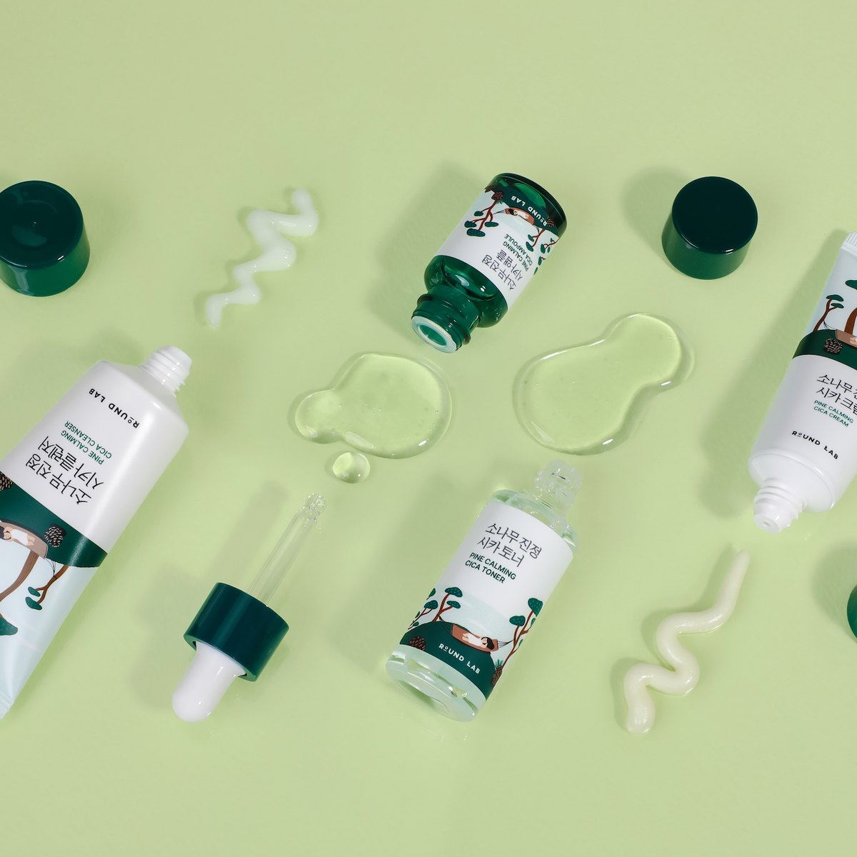As quatro miniaturas do kit Round Lab Pine Calming Cica deitadas ao lado de texturas do produto, fundo verde claro.